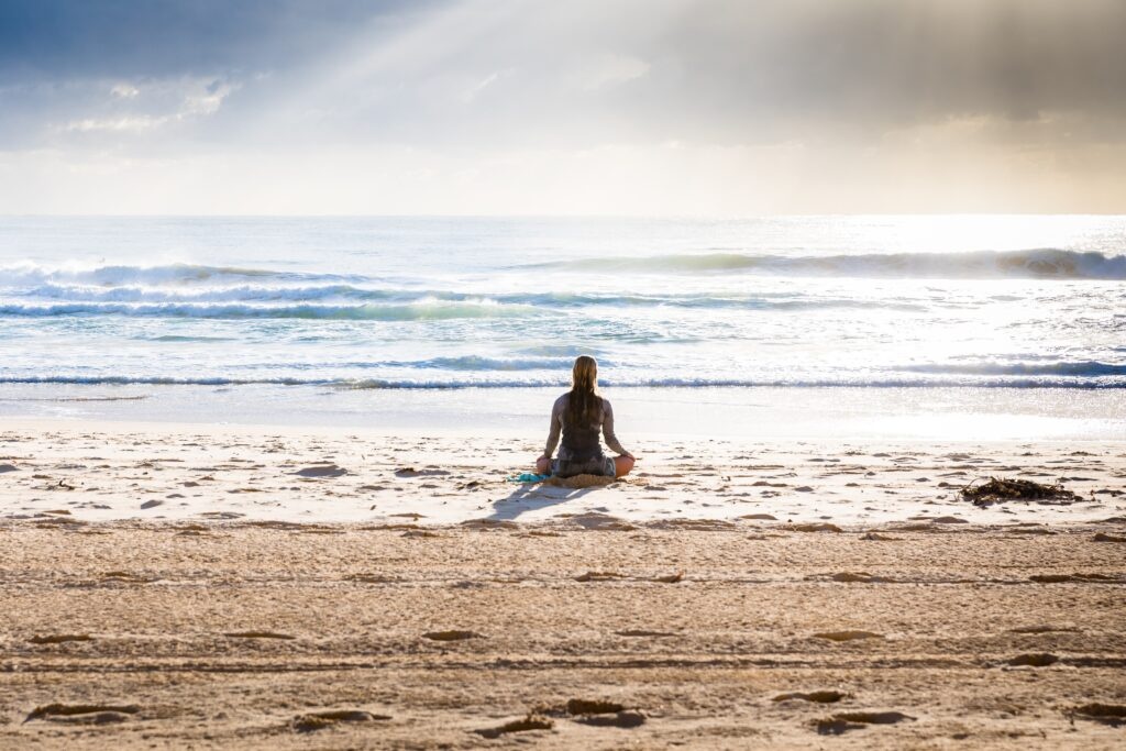 Kobieta relaksuje się podczas praktyki jogi na brzegu oceanu.