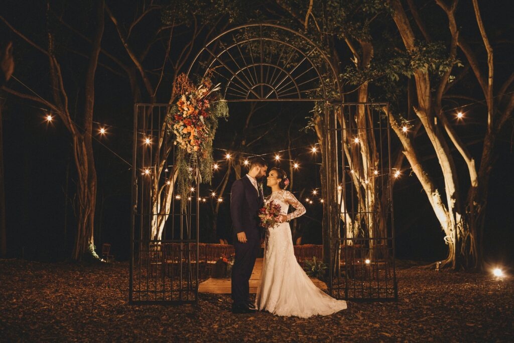 Para Młoda pozuje do zdjęcia na oświeconym lampionami plenerowym weselu. 