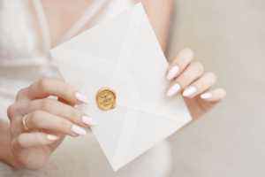 kobiece dłonie trzymające białą kopertę z zaproszeniem ślubnym